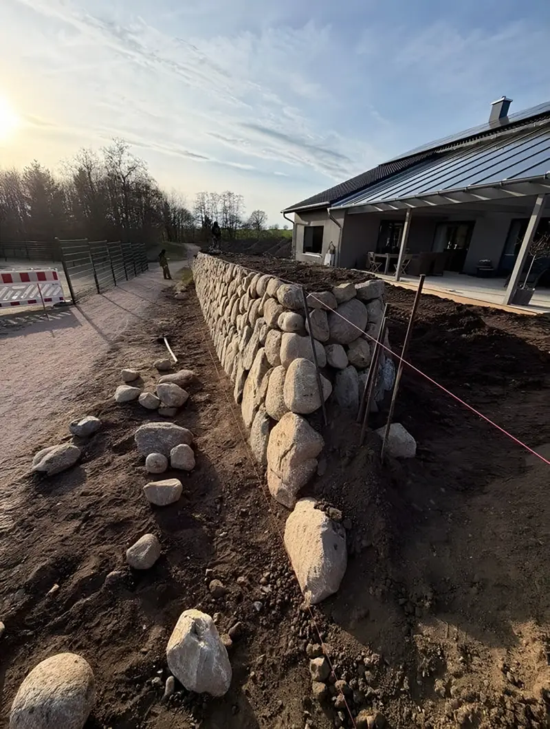 Baustelle: ein Friesenwall wird gesetzt, davor liegen sortierte Feldsteine auf dem ausgehobenen Boden