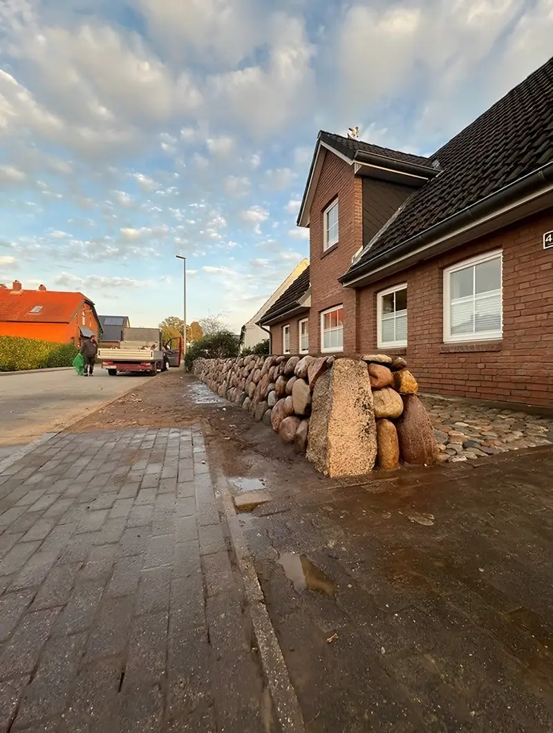 Neu gesetzter Friesenwall mit großem Eckstein an der Straßenseite eines Backsteinhauses