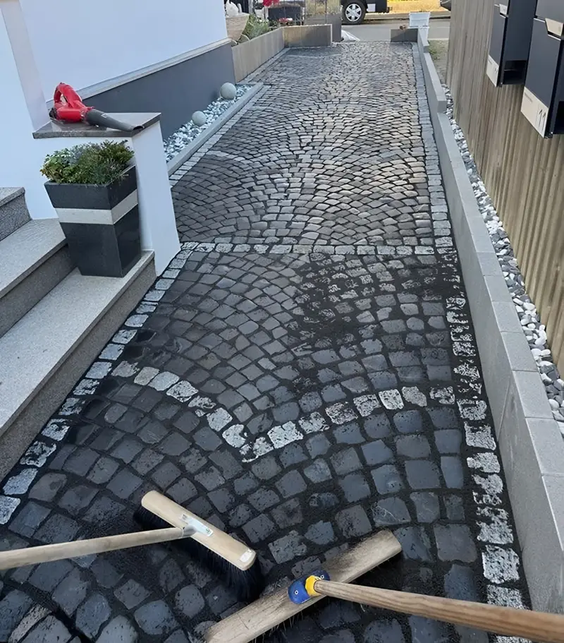 Hauszugang aus dunklem Natursteinpflaster, in Bögen verlegt, mit hellen Zierreihen und Einfassung aus Granit