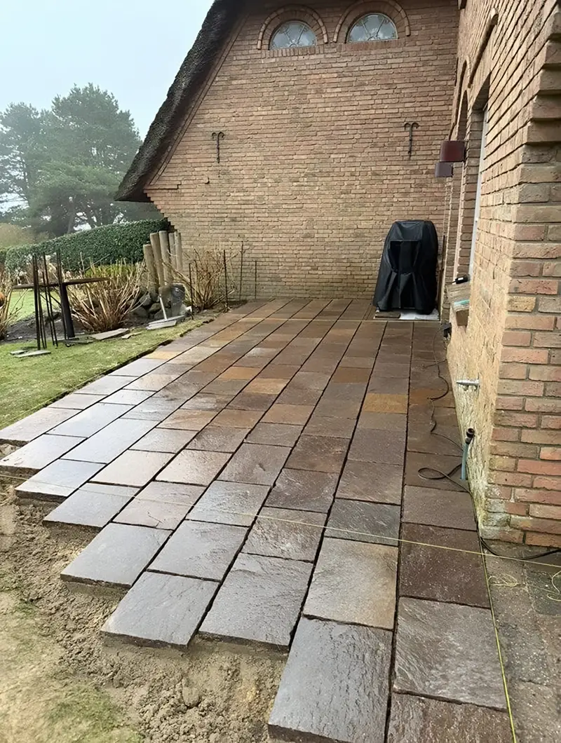 Terrassenplatten werden an einem Backsteinhaus verlegt, die vordere Reihe liegt noch offen im Sandbett