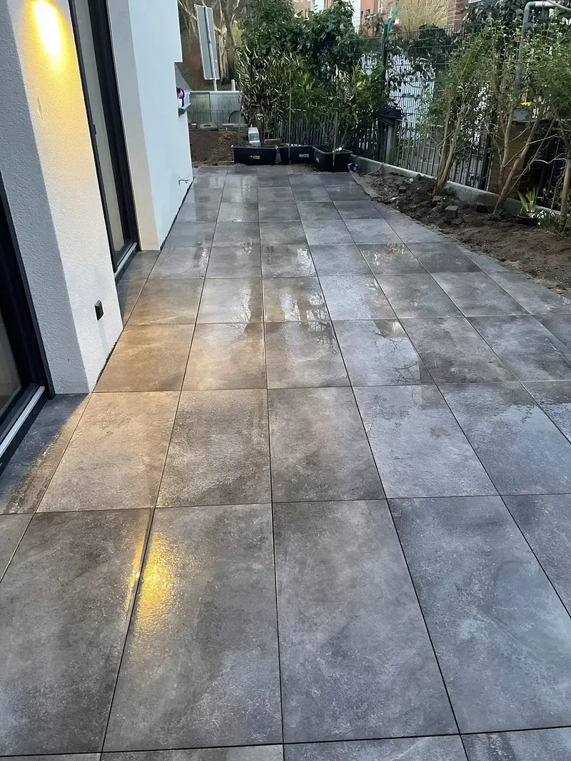 Terrasse aus großen grauen Platten entlang einer Hausfassade mit bodentiefen Fenstern