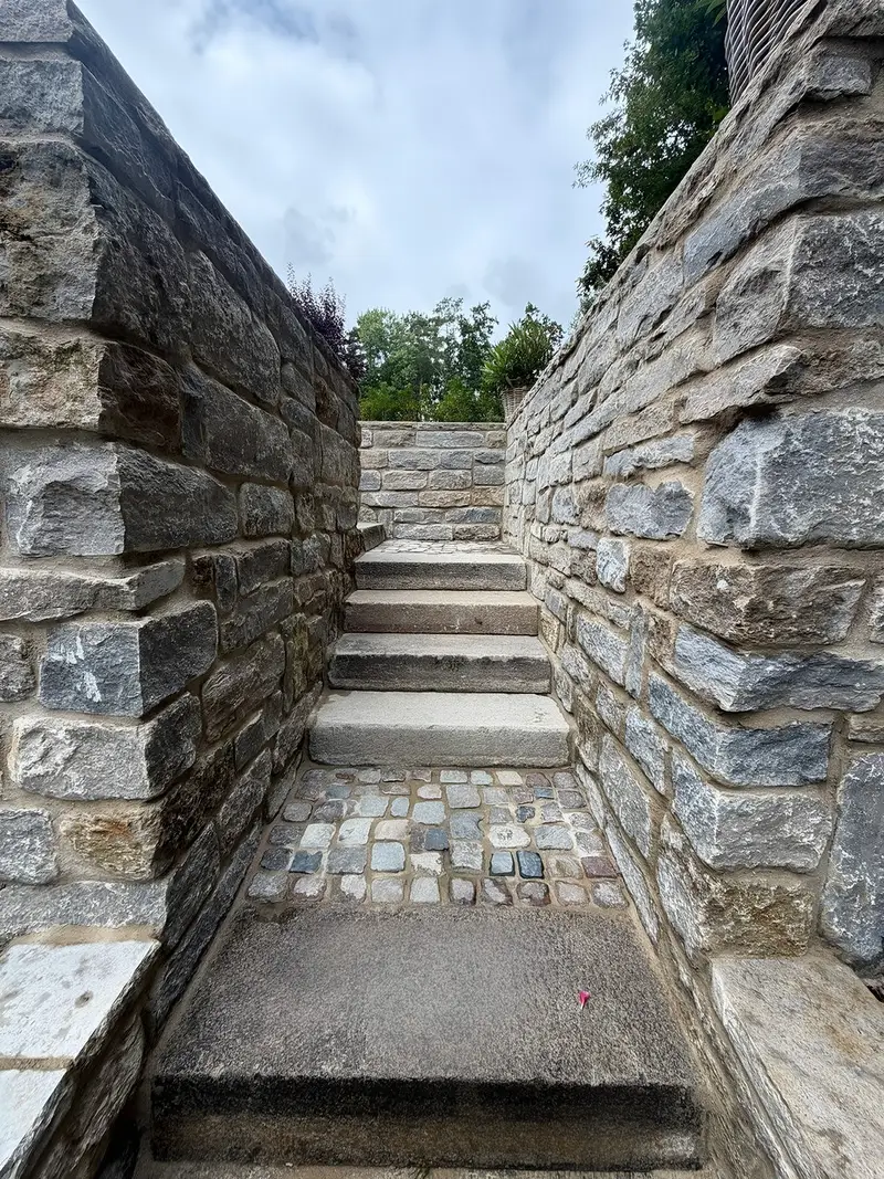 Treppe aus Granitstufen, die zwischen zwei hohen Mauern aus gespaltenem Naturstein nach oben führt
